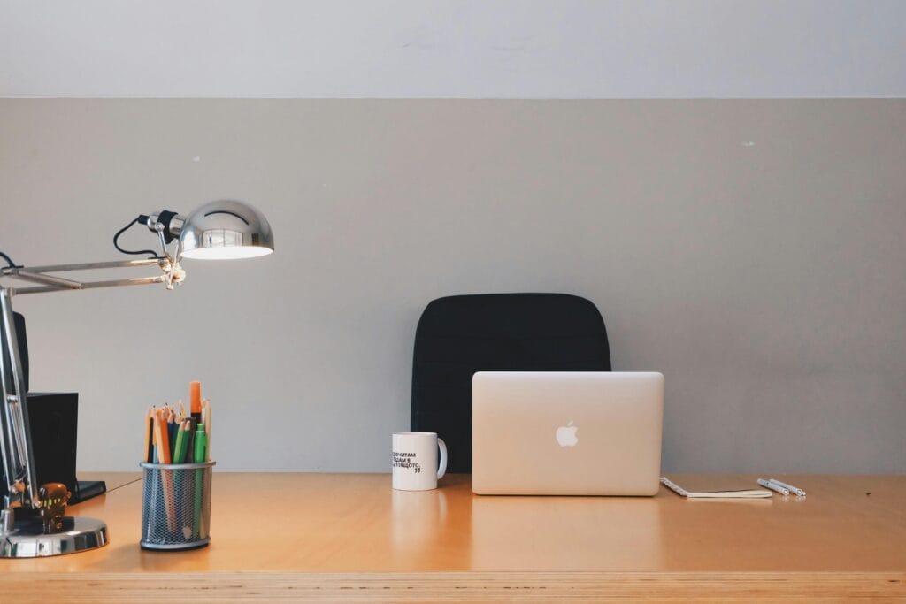 A tidy minimalist office setup featuring a laptop, desk lamp, and stationery.