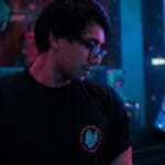 Stylish young man with glasses in a moody, neon-lit environment.